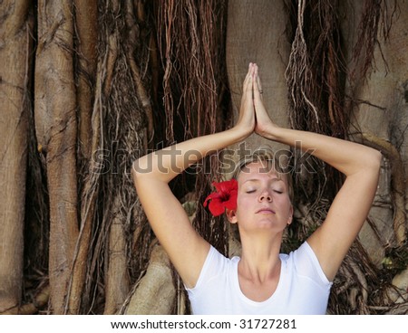 Woman in white meditating in front of Bodhi Tree Roots with red flower