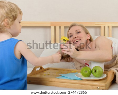 Son gives mom a flower. Mother lying on the bed , next to a table for breakfast