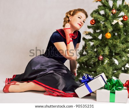 Woman sitting near a Christmas tree with gift in hand