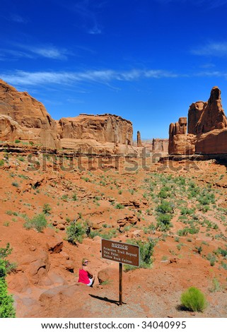 Woman Sits At Entrance to Park Avenue in Arches National Park