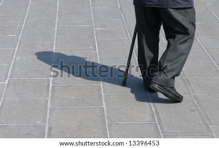 Legs detail of a senior man walking with help of a walking stick.