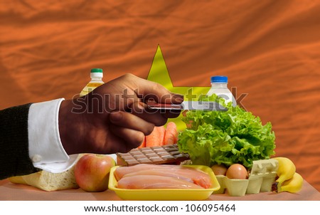 man stretching out credit card to buy food in front of complete wavy national flag of vietnam