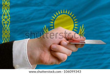 man stretching out credit card to buy goods in front of complete wavy national flag of kazakhstan