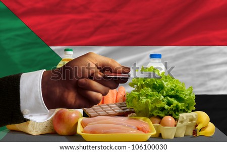 man stretching out credit card to buy food in front of complete wavy national flag of sudan