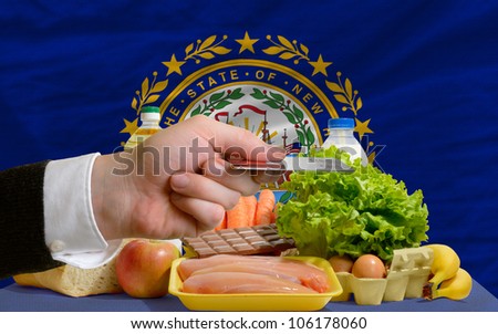 man stretching out credit card to buy food in front of complete wavy american state flag of new hampshire