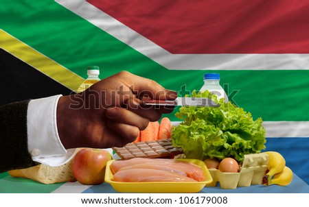 man stretching out credit card to buy food in front of complete wavy national flag of south africa