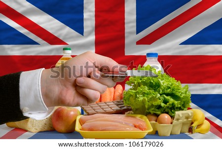 man stretching out credit card to buy food in front of complete wavy national flag of great britain