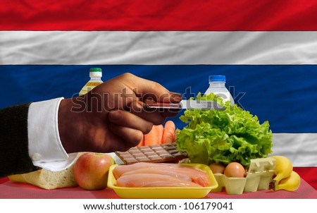 man stretching out credit card to buy food in front of complete wavy national flag of thailand