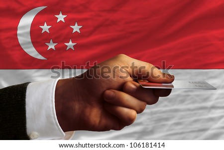 man stretching out credit card to buy goods in front of complete wavy national flag of singapore