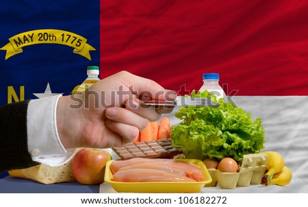 man stretching out credit card to buy food in front of complete wavy american state flag of north carolina