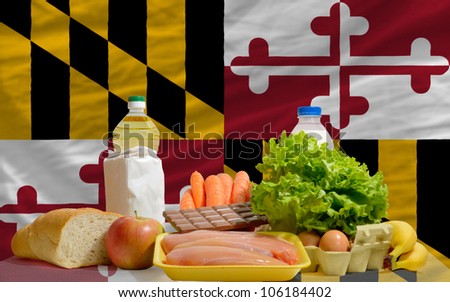 complete american state flag of maryland covers whole frame, waved, crunched and very natural looking. In front plan are fundamental food ingredients for consumers, symbolizing consumerism