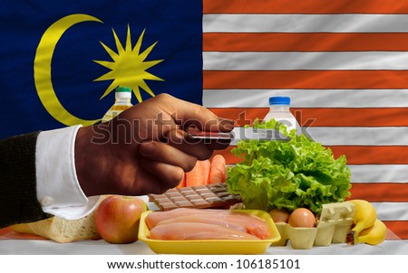 man stretching out credit card to buy food in front of complete wavy national flag of malaysia