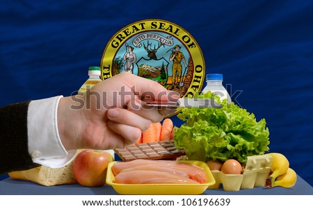 man stretching out credit card to buy food in front of complete wavy american state flag of idaho