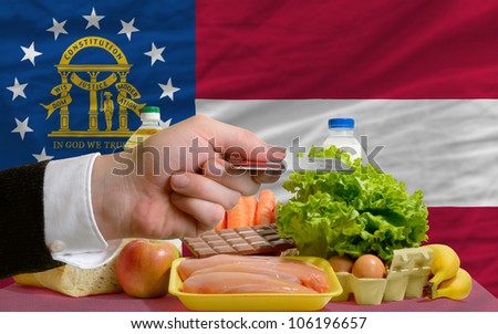 man stretching out credit card to buy food in front of complete wavy american state flag of georgia