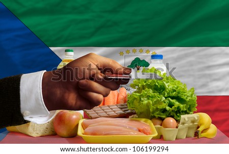 man stretching out credit card to buy food in front of complete wavy national flag of equatorial guinea