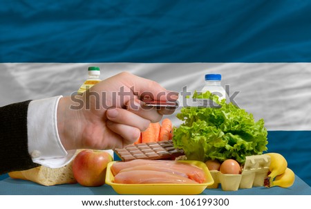 man stretching out credit card to buy food in front of complete wavy national flag of el salvador