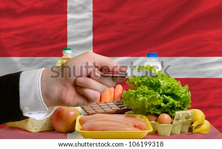man stretching out credit card to buy food in front of complete wavy national flag of denmark