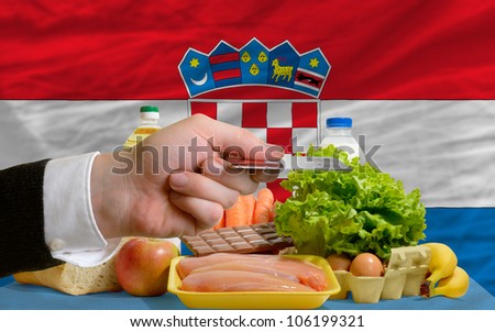 man stretching out credit card to buy food in front of complete wavy national flag of croatia