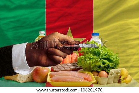 man stretching out credit card to buy food in front of complete wavy national flag of cameroon
