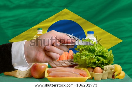 man stretching out credit card to buy food in front of complete wavy national flag of brazil