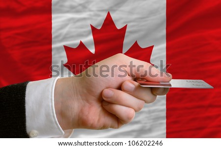 man stretching out credit card to buy goods in front of complete wavy national flag of canada