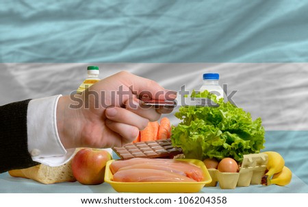 man stretching out credit card to buy food in front of complete wavy national flag of argentina