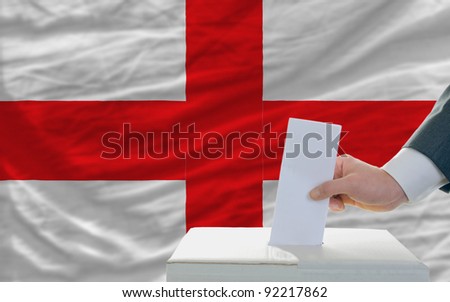man putting ballot in a box during elections in england in front of flag