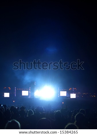 Large rock concert audience, blank screens and burst of light from the stage.