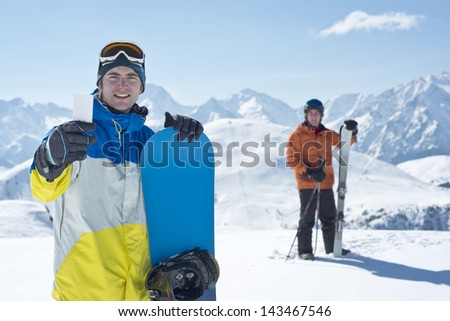 Two man with winter sport equipment looking at camera. One is showing a blank lift pass. Concept to illustrate ski admission fee