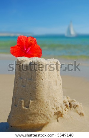 Sand Castle and Flower on Shore with Sailboat in Distance