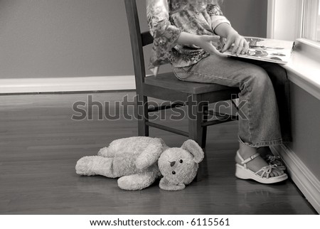 Young Girl Reading Book at Window with Stuffed Animal on Floor