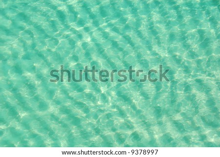 Aerial view of beautiful clear turquoise ocean water showing ripples in sand with sparkling sunlight