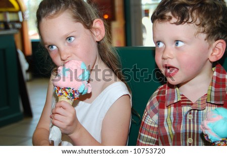 Cute boy and girl eating huge cones in ice cream parlor