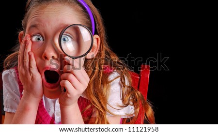 Young school girl looking through magnifying glass looking shocked at what she sees