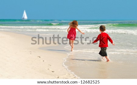 Kids running on pretty beach with sailboat  in distance