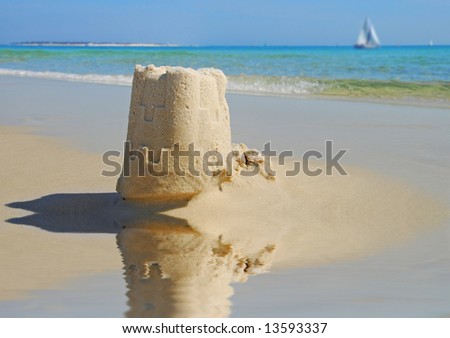 Pretty sand castle by tidepool with sailboat on ocean in distance