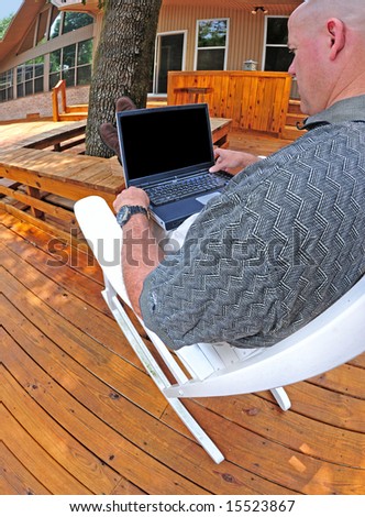 Man relaxing in rocker working on laptop computer on outside deck