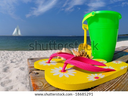 Colorful flip flops, beach pail, and shells on boardwalk by ocean