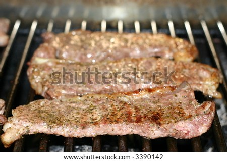 Three strip steaks cooking on the grill