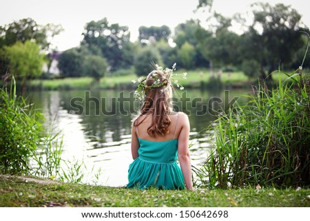 girl in a wreath sitting on the river bank