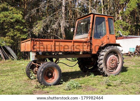 Old red agriculture tractor in farm. Pine forest in summer