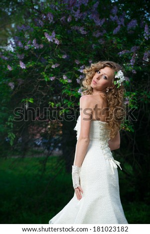 Beautiful bride in a white dress on a lilac background in spring. Professional make-up and hairstyle.