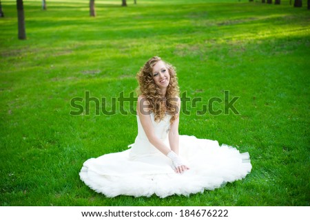 Beautiful bride in a white dress on green grass in summer. Professional make-up and hairstyle.