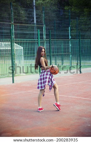 Beautiful young woman playing basketball outdoors.  The girl on the sports ground