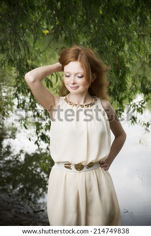 Portrait of redhead girl with blue eyes on nature. Young woman in a dress standing near the tree