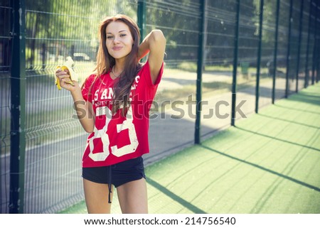 Beautiful young woman on the sports ground. Girl eating a banana