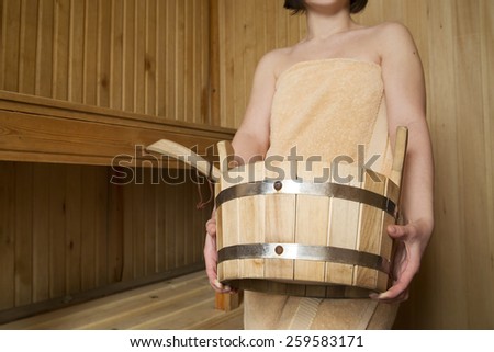 Beautiful woman in sauna, bath accessories. Wooden bucket and sticks