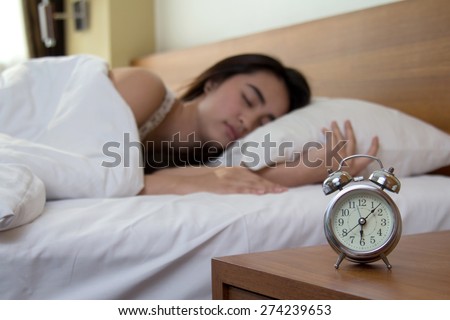 woman asleep in bed while her alarm shows the early time at home in bedroom