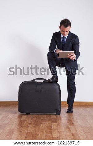 Businessman sit on a travel luggage using a digital tablet