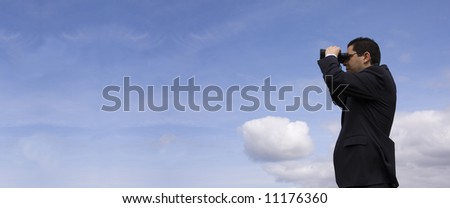 Businessman looking through binoculars with a blue sky as background (panoramic photo)